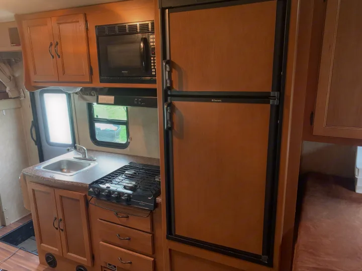 Inside an RV rental: a practical kitchen with wood cabinets, sink, gas stove, microwave, and a large refrigerator.. Other Other 2014