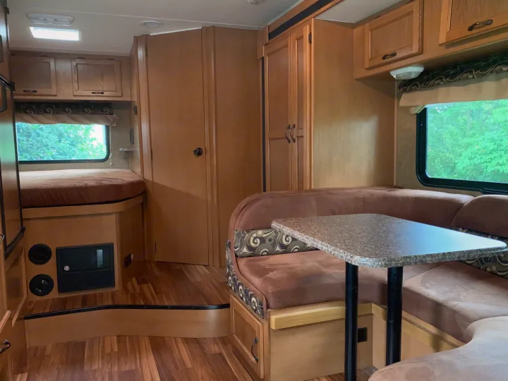 This rv rental interior offers a bed, dinette with table, and wood cabinetry, ideal for comfortable road trips.. Other Other 2014