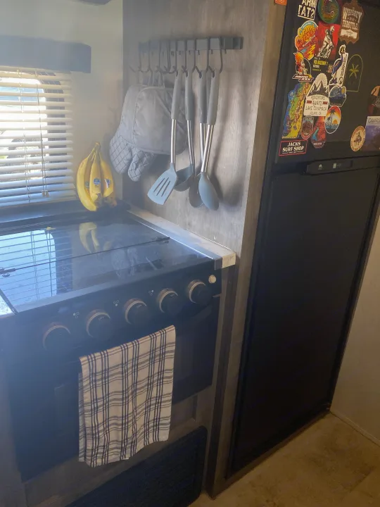 Compact RV rental kitchen, featuring a stove, fridge with travel stickers, bananas, and hanging utensils.. Forest River Vengeance 2021