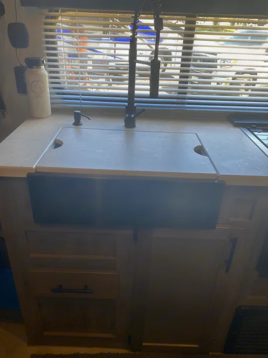 RV rental kitchen: A light countertop features a covered sink, black faucet, soap dispenser, and window with blinds.. Forest River Vengeance 2021