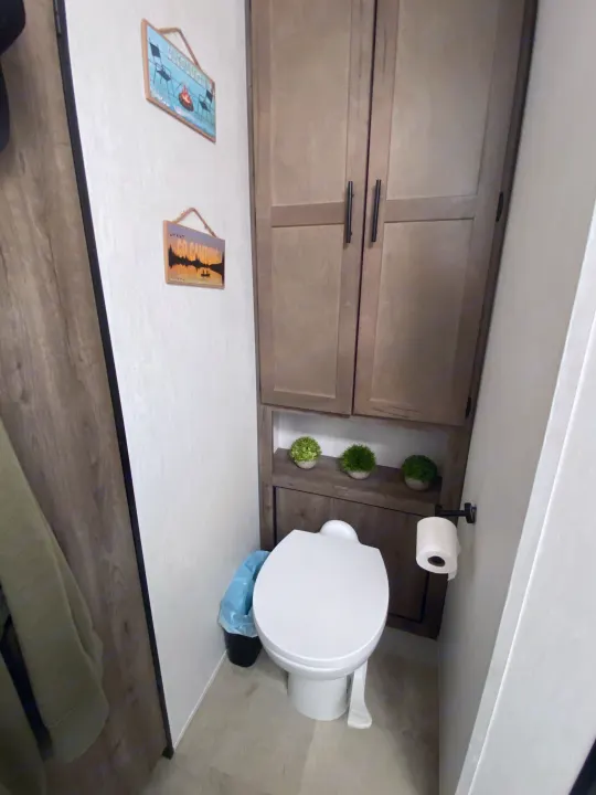 Compact RV rental bathroom features a toilet, overhead storage cabinets, and charming camping-themed decor on the wall.. Forest River Vengeance 2021