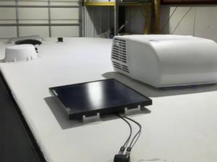 On an RV rental roof, a black solar panel and white antenna dome are visible next to a large air conditioner unit.. Forest River Cherokee Alpha Wolf 2022