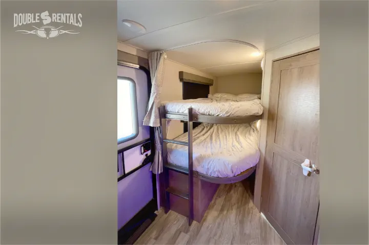 Cozy bunk beds with bedding, a ladder, and a window visible inside this RV rental, perfect for family camping.. Grand Design Imagine 2021