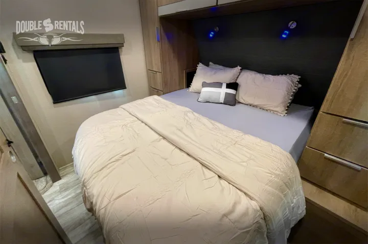 Cozy RV rental bedroom with a made bed, decorative pillows, built-in storage on both sides, and ambient blue reading lights.. Grand Design Imagine 2021