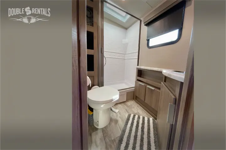 RV rental bathroom featuring a white toilet, glass shower, and wood vanity with a sink, all in a compact, functional space.. Grand Design Imagine 2021