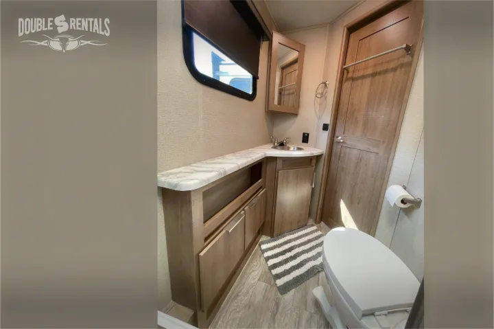 Clean RV rental bathroom features a vanity, sink, mirror, toilet, and window with a shade.. Grand Design Imagine 2021