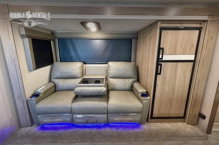 RV rental features a cozy living space with Thomas Payne reclining theater seating, blue underglow LEDs, and fridge.. Grand Design Imagine 2021