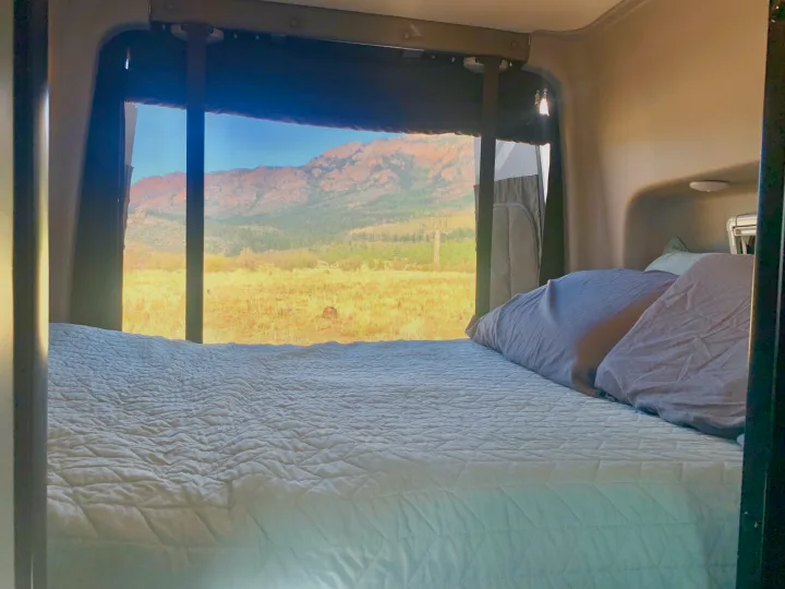 RV rental bedroom with a comfy bed and a stunning view of golden fields and mountains from the large window.. Winnebago Revel 2021