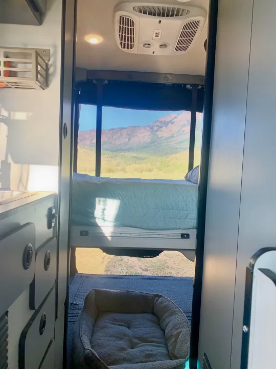 Cozy RV rental interior: a bed and dog bed overlook a stunning mountain vista through the rear window. Perfect for adventure.. Winnebago Revel 2021