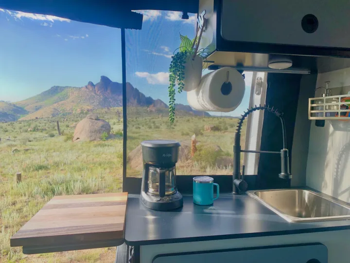 Serene desert mountain view from inside an RV rental. A cozy kitchen setup with coffee, perfect for remote adventures.. Winnebago Revel 2021