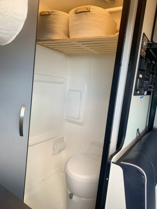 Inside an RV rental, showing a compact wet bath with toilet, shower area, and stylish overhead storage.. Winnebago Revel 2021
