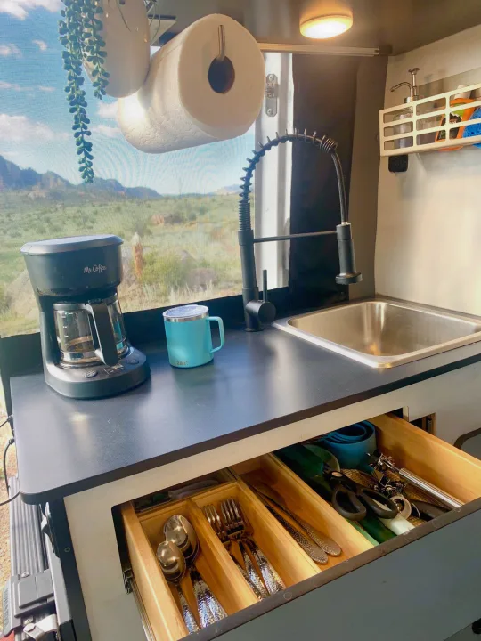 Bright RV rental kitchen with Mr. Coffee, sink, and organized drawers. Window view of mountains and sky.. Winnebago Revel 2021