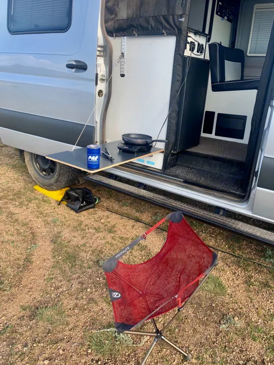 RV rental for outdoor cooking! This van offers an extended table with a stove, perfect alongside a red Moonlite camp chair.. Winnebago Revel 2021