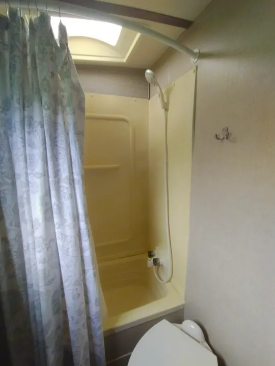 An RV rental's compact, beige shower stall and partial patterned curtain, with a shower head and small toilet visible.. Dutchmen Aerolite 28dbhs 2017