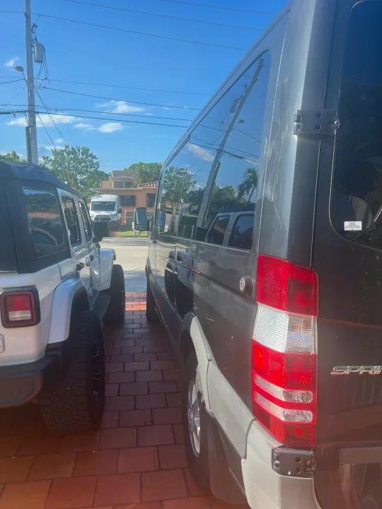 A white Jeep is parked beside a dark gray Sprinter van, ideal for an rv rental, on a brick driveway under a sunny sky.. Mercedes Sprinter 2016