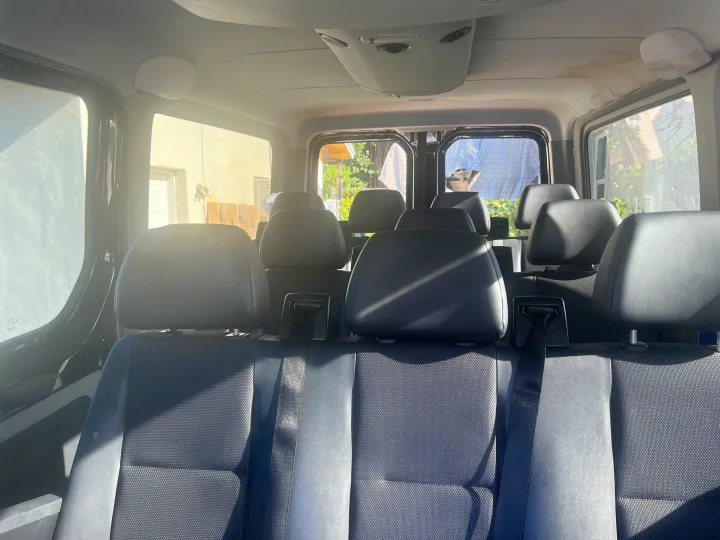 Inside an RV rental vehicle, rows of black seats with fabric upholstery are visible, bathed in sunlight from the side windows.. Mercedes Sprinter 2016