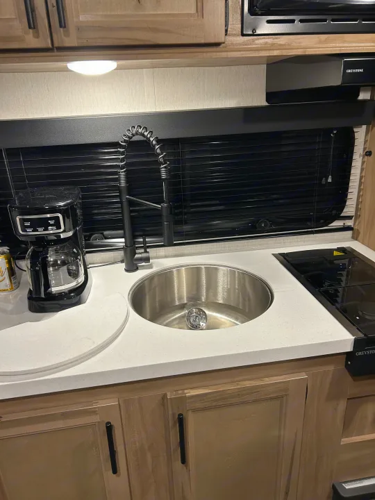 Compact kitchen counter in an RV rental, featuring a stainless steel sink, modern black faucet, coffee maker, and built-in stove.. Forest River Wolf Pup 16 BHS Black Label 2023