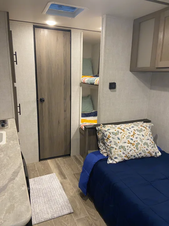 Cozy RV rental interior featuring a bedroom, bunk beds, and partial kitchen. Ideal for family adventures.. Gulf Stream Enlighten 2021