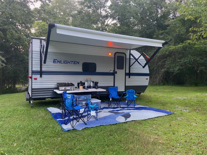 Enjoying an RV rental campsite: travel trailer with extended awning, outdoor kitchen, chairs, and mat on grass.. Gulf Stream Enlighten 2021