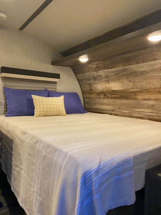 Cozy RV rental bedroom featuring a comfy bed with striped blanket, blue & yellow pillows, and wood accent walls.. Gulf Stream Enlighten 2021