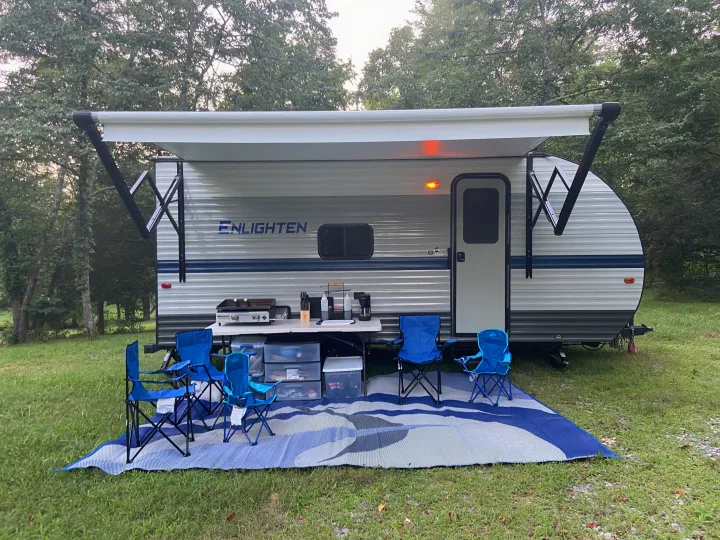 RV rental: A cozy travel trailer with an extended awning, outdoor kitchen, chairs, and mat set up for camping.. Gulf Stream Enlighten 2021