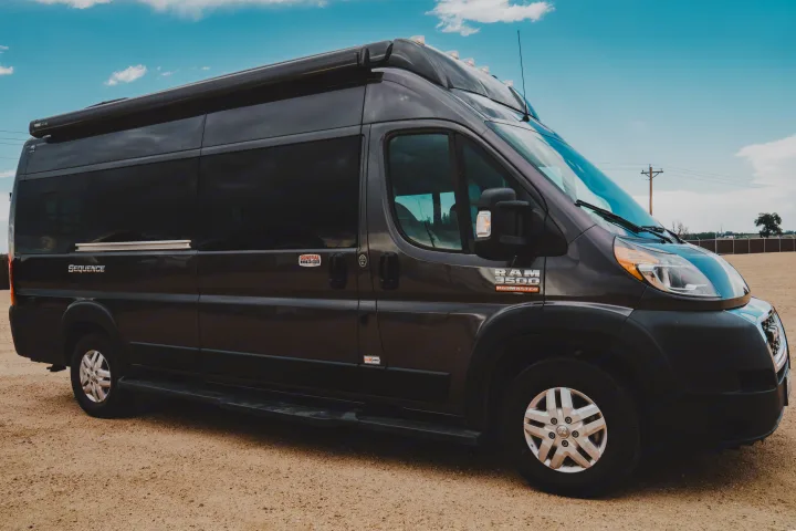 Dark gray Thor Motor Coach Sequence camper van (RAM ProMaster), an excellent RV rental, parked on dirt under a blue sky.. Thor Motor Coach sequence 2021