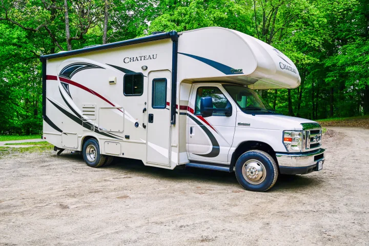 White Thor Chateau Class C RV rental parked on a dirt path amidst lush green trees, perfect for your next outdoor adventure.. Thor Chateau 2017