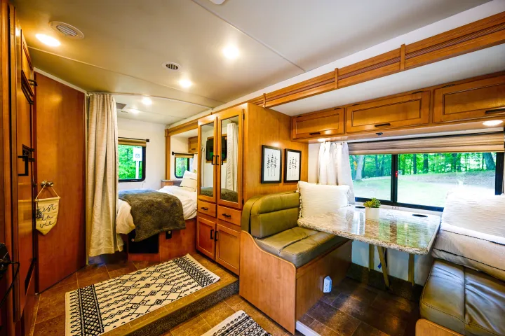 Bright rv rental interior: cozy bedroom, dinette, wooden cabinets, and large window with nature views, great for your camper trip.. Thor Chateau 2017
