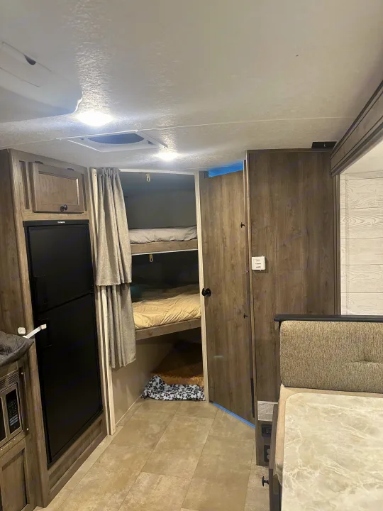 RV rental interior showcasing space-saving bunk beds with privacy curtains, compact kitchen appliances, and a comfortable dinette.. Coachmen Apex Nano 2021