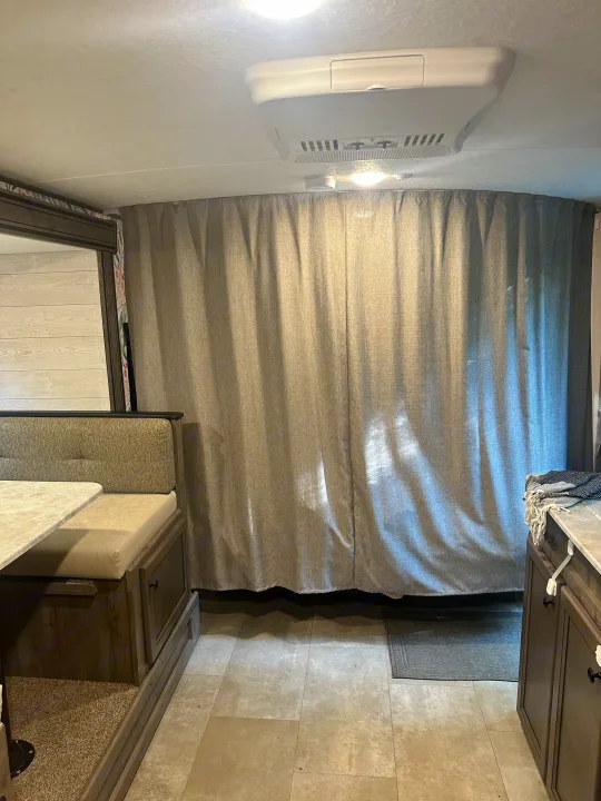 Spacious RV rental interior with a dining booth, a full-width gray privacy curtain, and a kitchen counter.. Coachmen Apex Nano 2021