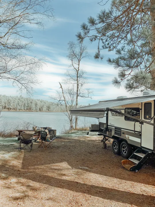 Our rv rental parked at a tranquil lakeside campsite with a picnic table, chairs, and fire pit ready for adventure.. Coachmen Apex Nano 2021