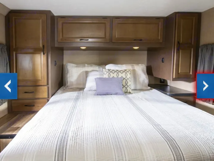 Cozy **RV rental** bedroom showing a bed with striped bedding, overhead lights, and wood-look storage cabinets.. Thor Majestic 2018