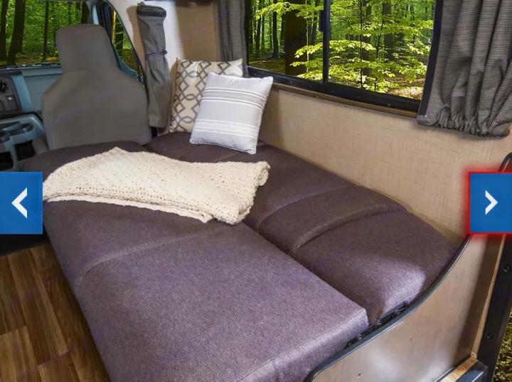Experience comfort in your RV rental! This interior features a cozy bed/lounge area with pillows, blanket, and a scenic nature view.. Thor Majestic 2018
