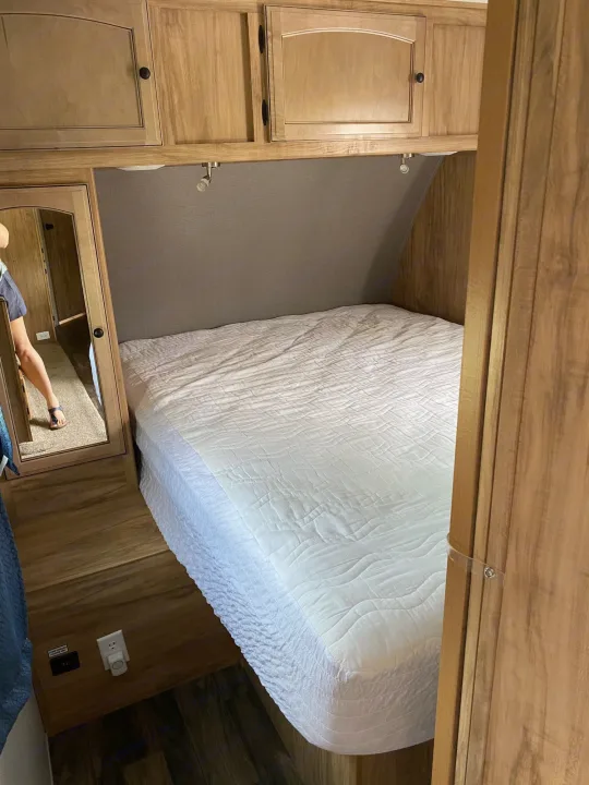 Cozy RV rental bedroom featuring a white bed, overhead cabinets, and mirror. Ideal for compact travel.. Coachmen Freedom Express 2018