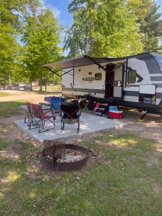 An RV rental is set up at a pleasant campsite with an awning, chairs, and a fire pit, ready for outdoor fun.. Crossroads RV Zinger Lite 2021