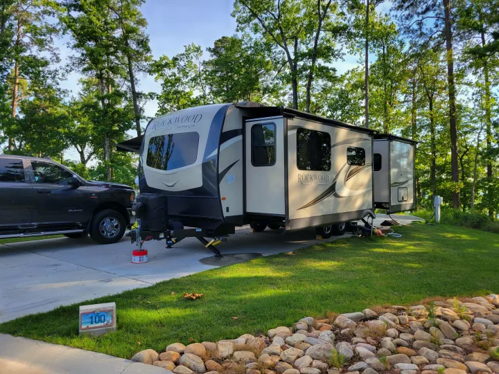 An RV rental, a Rockwood travel trailer, parked at campsite 100 with a truck, surrounded by lush trees.. Forest River Rockwood Ultra Lite 2020