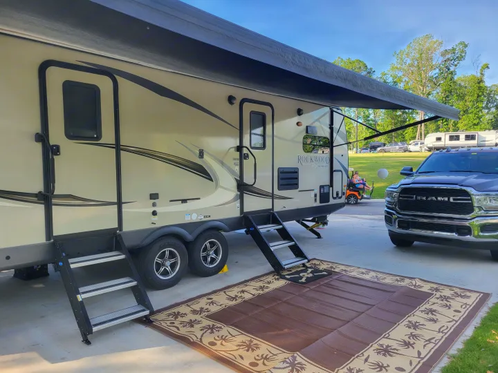 Enjoying an RV rental: Rockwood travel trailer with awning, steps, and outdoor mat at a sunny campsite. Truck parked.. Forest River Rockwood Ultra Lite 2020
