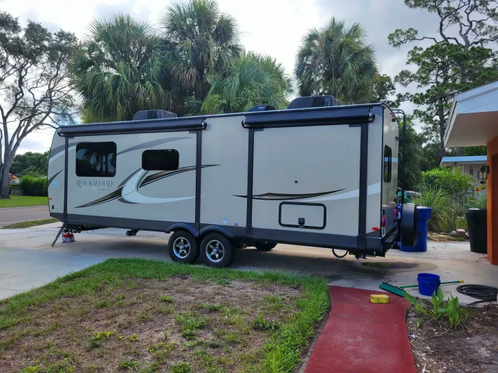 This Rockwood travel trailer, an RV rental, is parked in a driveway amidst lush greenery, ready for its next trip.. Forest River Rockwood Ultra Lite 2020