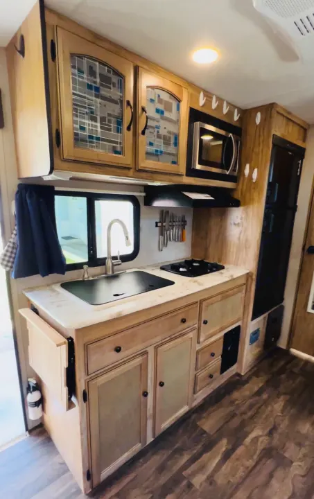 Bright RV rental kitchen with wood cabinets, sink, stove, microwave, and fridge. Compact yet fully equipped for travel.. Coachmen Other 2019