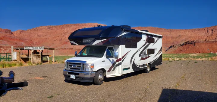 An Esteem Entegra RV rental parked on gravel, with a Navajo jewelry stand and red rock landscape under a clear blue sky.. Entegra Coach Esteem 2021