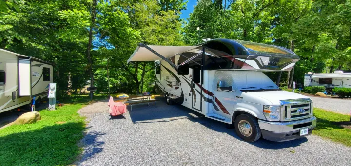 Sunny campsite with an Esteem Entegra RV rental featuring an extended awning, picnic table, and utility hookups. Perfect for outdoor getaways.. Entegra Coach Esteem 2021
