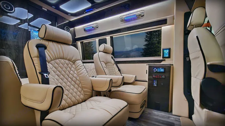This luxury RV rental interior boasts plush, quilted cream seats, dark wood accents, and scenic window views.. Ultimate Toys Ultimate Coach 2023