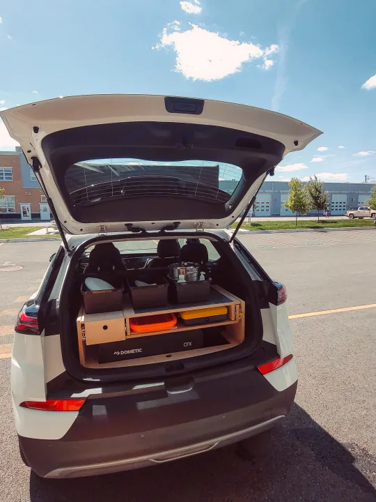 White SUV trunk open, revealing a custom modular car camping kitchen with Dometic cooler. An agile RV rental alternative.. Chevrolet Other 2023