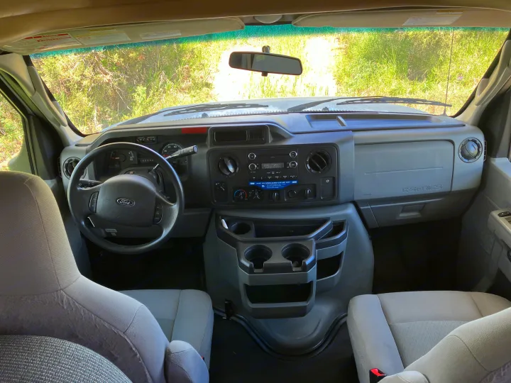 Inside an RV rental Ford E-Series van, showing the dashboard, steering wheel, seats, and view ahead on a dirt road.. Majestic Ford 2018