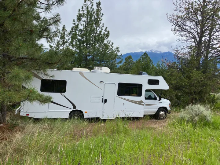 An rv rental is nestled among pine trees, with majestic snow-capped mountains visible in the distance.. Majestic Ford 2018