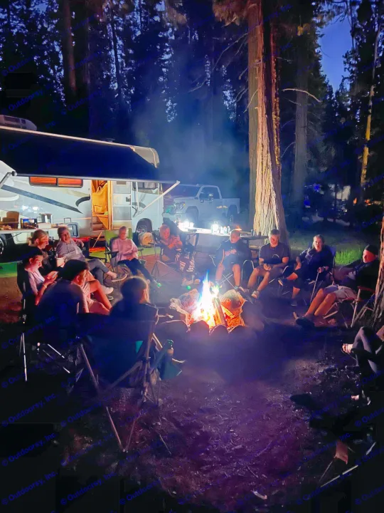 Night camping with friends around a warm campfire, next to an RV rental under tall trees.. Four Winds Hurricane 2002