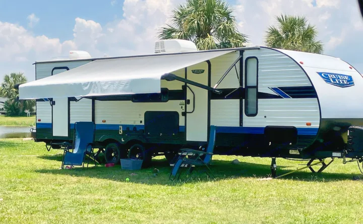 An RV rental, a white and blue travel trailer with awning out, set up for camping on green grass near palm trees.. Forest River Salem Cruise Lite 2023