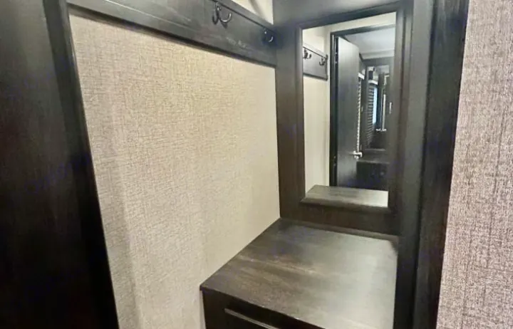 Inside your RV rental: a practical entryway with dark wood trim, coat hooks, mirror, and counter space for convenience.. Jayco White Hawk 2021