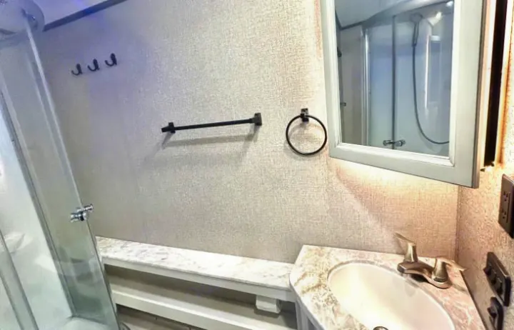 This modern RV rental bathroom features a sink, mirror, shower, towel bar, ring, and hooks. Compact and functional.. Jayco White Hawk 2021