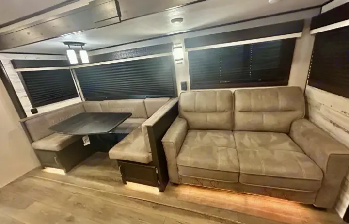 Spacious RV rental interior: a light gray U-shaped dinette, sofa, and warm under-lighting for comfortable travel.. Jayco White Hawk 2021